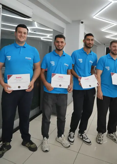 Dört katılımcı, ellerindeki eğitim sertifikalarını göğüs hizasında tutarak yan yana duruyor. Belgelerin üzerinde 'EĞİTİM SERTİFİKASI' başlığı ve katılımcı adı yazılı.