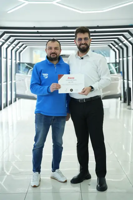 Belgede program “PPF Kaplama” olarak geçiyor. Metin, eğitimin uygulama merkezinde yapıldığını söylüyor.

Kare, sertifika takdimlerinin çekildiği koridorun aydınlık ucunda alınmış.