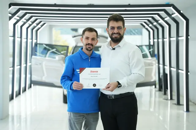 Aynı takdimin başka bir karesinde belge iki kişi tarafından birlikte tutuluyor; başlık “EĞİTİM SERTİFİKASI” olarak okunuyor.

Katılımcı bilgisi elle değil baskıyla yer alıyor — belge tek tek düzenleniyor, boş forma sonradan yazılmıyor.