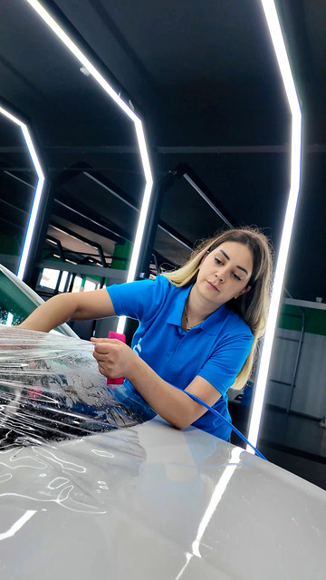 PPF kaplama eğitiminde kadın kursiyerimiz kaputa uyguladığı şeffaf filmi ortadan kenarlara doğru konumlandırıyor.