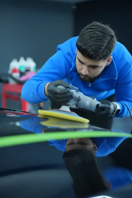 Makine, panelin kenar hattına yakın bölgede çalışıyor; kenar boyunca yeşil koruma bandı çekilmiş. Boya en ince yerde, yani kenar ve kabartılarda durur; makine buraya geldiğinde devir ve baskı düşürülür, bant ise hataya karşı ikinci güvenliktir.