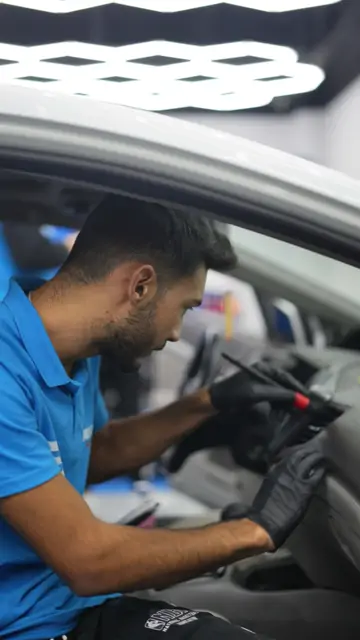 Sürücü koltuğuna oturmuş bir kişi, eldivenli eliyle detay fırçasını torpido ve havalandırma ızgaralarında gezdiriyor. Izgara aralarındaki toz bezle alınamaz; önce fırçayla gevşetilir, sonra yüzeyden toplanır.