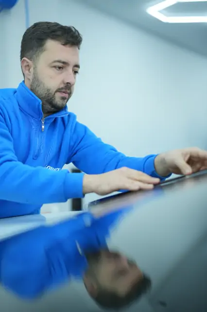 Boyalı panelin kenar hattı boyunca eller düz gezdiriliyor; yüzeydeki yansıma insan siluetini net veriyor. İşleme başlamadan önce yüzeyin elle okunması, hangi bölgenin ne kadar müdahale isteyeceğini belirler.