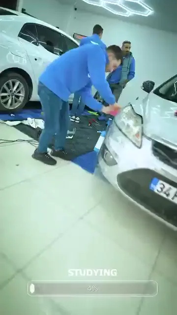 Beyaz bir aracın ön bölümüne film uygulanışı baştan sona hızlandırılmış olarak izleniyor; alttaki "STUDYING" çubuğu yüzde yüze doğru ilerliyor.

Kareler işin sırasını veriyor: yüzeyin spreyle ıslatılması, filmin panele yatırılması, raglenin altındaki suyu sıyırması, kenarlarda ısı tabancasıyla oturtma.

Çalışma tek kişilik değil; aynı aracın çevresinde birkaç kişi aynı anda ilerliyor.
