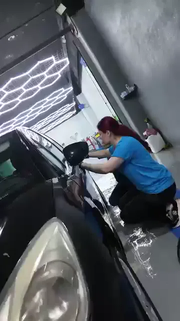 Koyu renkli bir aracın panel kenarları önce mavi maskeleme bandıyla ayrılıyor, ardından makineli polisaja geçiliyor. Katılımcılar makineyi kaput, kapı ve çamurluk üzerinde bölge bölge gezdiriyor; bir bölümde sarı aplikatörle elle çalışılıyor, aralarda yüzey mikrofiberle siliniyor.