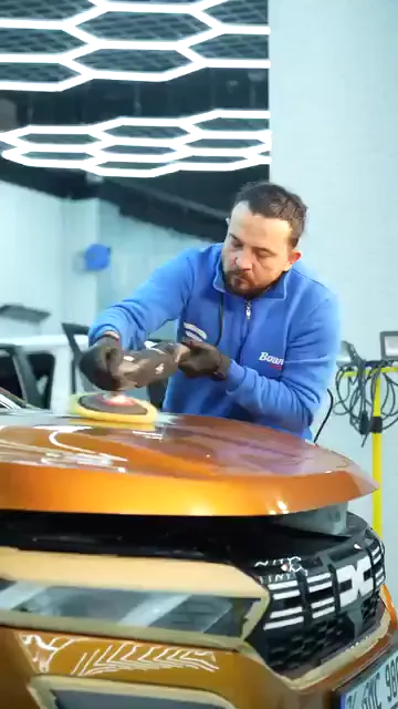 Eldivenli bir usta makinenin hem gövdesini hem ön tutamağını kavrayarak turuncu kaputun üzerinde ilerliyor. Kollar dirsekten kırılmıyor, makinenin ağırlığı iki el arasında dengeleniyor ve ped yüzeye düz basıyor. Tek elle bastırılan makine yüzeyde eşit iz bırakmıyor; buradaki tutuş bunun önüne geçiyor.