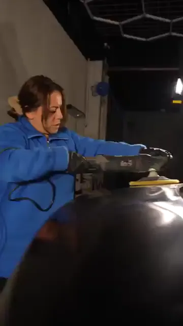 Işığın azaldığı bir bölümde saçı toplanmış bir kadın, koyu renk panelin üzerinde sarı pedli makineyi çalıştırıyor. Makinenin gövdesini iki eliyle kavrıyor, kolları omuz hizasında sabit kalıyor. Panelin kavisli yüzeyinde ped düz kalacak biçimde tutuluyor.