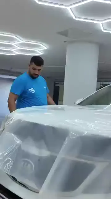 Doğru konum bulunmadan film yüzeye bırakılmıyor; parça önce panelin üstünde iki elle hizalanıyor. Islatılan panelde film turuncu ragle ile ortadan kenara doğru sıvazlanıyor, tekerlek davlumbazı gibi dönüşlerde esnetilerek oturtuluyor. Şeffaf filmde en çok göze batan hata kenarda kalan hava değil, yanlış hizalanmış ilk temastır.
