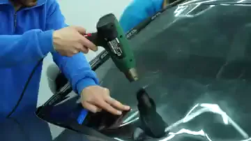 Bir el yeşil gövdeli ısı tabancasını camın üzerine serilmiş filme tutuyor, diğer el mavi bir ragleyle filmi cama yatırıyor. Isı verildikçe filmin kabaran bölgeleri toplanıp camın kavisine oturuyor. İşlem camın dış yüzeyinde yürütülüyor; film biçimini burada alıyor.