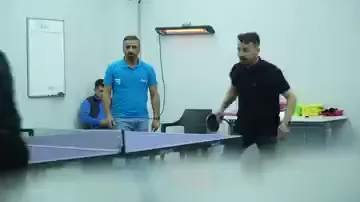 Beyaz tahtanın ve duvara asılı ısıtıcının bulunduğu odaya mavi bir masa tenisi masası kurulmuş. Mavi tişörtlü bir kişi ile siyah tişörtlü bir kişi karşılıklı vuruşuyor, arkadaki sırada oturan biri oyunu izliyor. Masa, sınıf düzeninin yerine geçmemiş; sıraların hemen yanına açılmış.