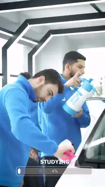 Beyaz aracın kapısında iki kişi birlikte çalışıyor: biri sprey şişesiyle yüzeyi ıslatıyor, diğeri pembe ragleyi filmin üzerinde gezdiriyor. Arka planda “paint protection” yazılı pano duruyor; ilerleyen karelerde çamurluk kenarında aynı işlem parmak ucuyla düzeltilerek sürüyor. Kayıtta konuşma yok.