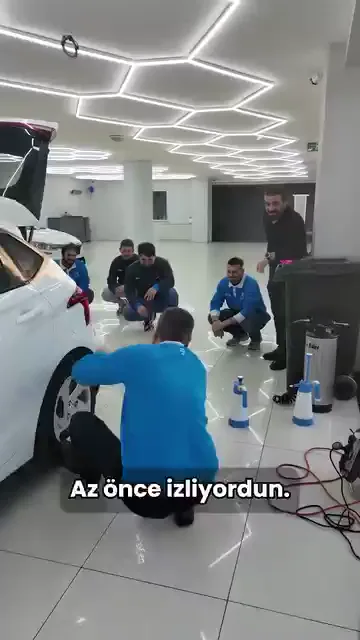 Uygulama alanında bir grup izlerken soru tersine çevriliyor: "Sen diyorsun ki potlar gitmiyor." Cevap hemen arkasından geliyor — "Hep aynı şeyi yapıp farklı sonuç beklemezsin."

İlk düzeltme duruşta. Araca yaklaşmak ve duruşu işle bütünlemek isteniyor; uzaktan, zorlanarak yapılan hamle malzemeyi oturtmuyor.

Karelerde arka tampon ve stop çevresine şeffaf film çekiliyor, öğrenciler işlemi çevresinde izliyor.

Potun sebebi çoğu zaman malzemede değil, tekrarlanan aynı hamlede.