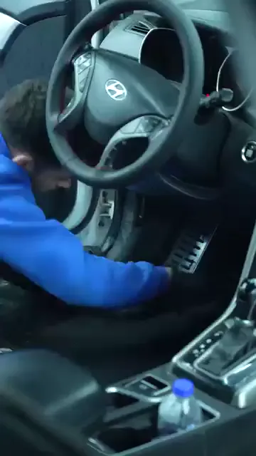 Kapısı açık bir aracın sürücü tarafında, eldivenli eller ayak bölgesindeki paspası kenarından tutup dışarı alıyor. Koltuk koruyucu kılıfla örtülmüş, pedal çevresi boşaltılmış durumda. Zemindeki çıkarılabilir parçalar alınmadan ayak bölgesine düzgün müdahale edilemiyor.