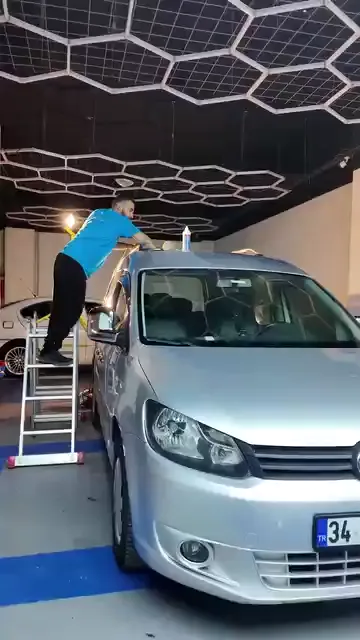 Tavana ulaşmak için merdiven kullanılıyor; makineye panelin üstünden değil, yandan yaklaşılıyor. Fitiller, çıtalar ve kapı kolu çevresi yeşil bantla kapatılmış durumda. Pasta şişesi ile mikrofiber bez panelin üstünde, çalışılan bölgenin hemen yanında duruyor.