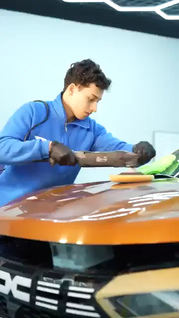 Genç bir katılımcı makineyi kaputun orta bölümünde, pastanın bırakıldığı alanda gezdiriyor. Hemen yanında katlanmış yeşil mikrofiber duruyor; ped döndükçe boyadaki yansıma çizgileri kısalıp uzuyor. Pasoyu bitirdiği alanda yansıyan ışık kesintisiz bir hat hâline geliyor.