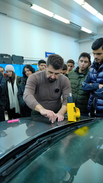 Lokman İn, PPF kaplamanın kaputa nasıl yapıldığını Ege Üniversitesi öğrencilerine gösteriyor.