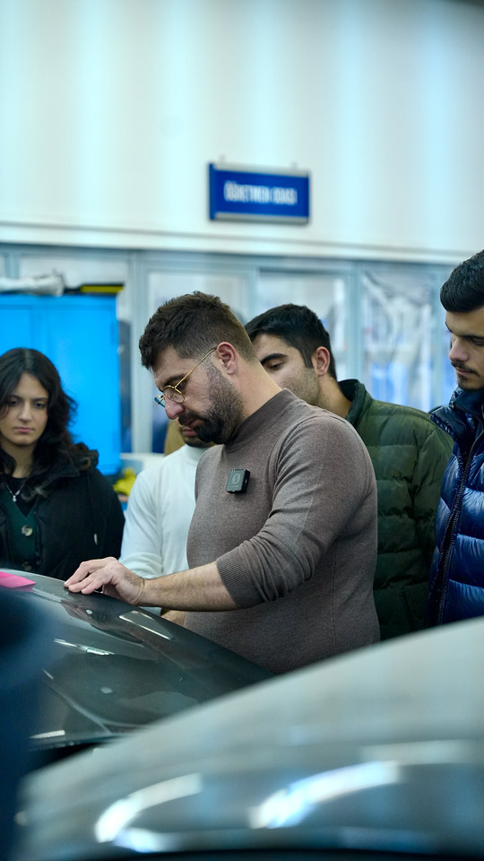 Lokman İn, PPF kaplamanın kaput üzerinde nasıl yapıldığını Ege Üniversitesi öğrencilerine uygulayarak gösteriyor.